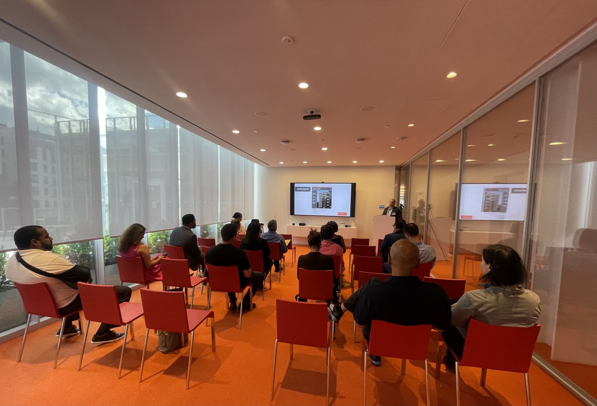 The CU Grow Vendor Development program hosted its first in-person procurement event since the beginning of the pandemic at The Forum at Columbia on June 9. A room with tall windows, 15 participants sitting in red chairs and a presenter standing at the front of the room in front of a large tv screen with powerpoint presentation.